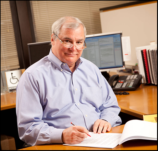 portrait of John Catlin at work desk with pen in hand